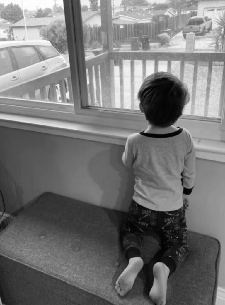 A young boy looking out the window on a rainy day.